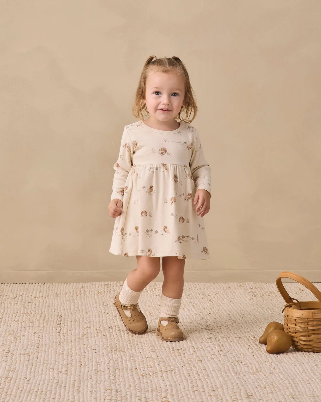 Baby girl wearing a cream long sleeve dress by Quincy Mae, featuring a soft fabric and simple, comfortable design.
