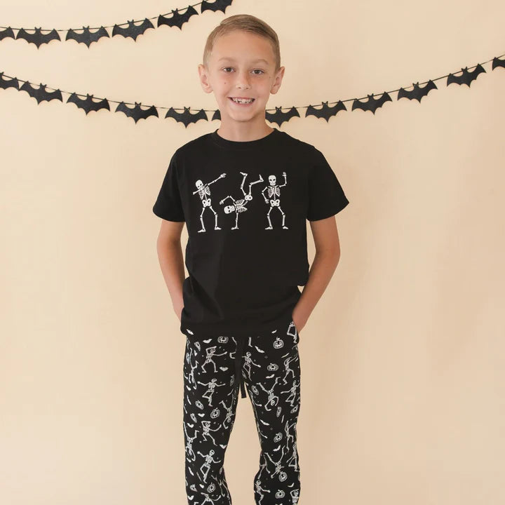 Model wearing Sweet Wink glow-in-the-dark Silly Skelly Halloween short sleeve T-shirt featuring a playful skeleton design.