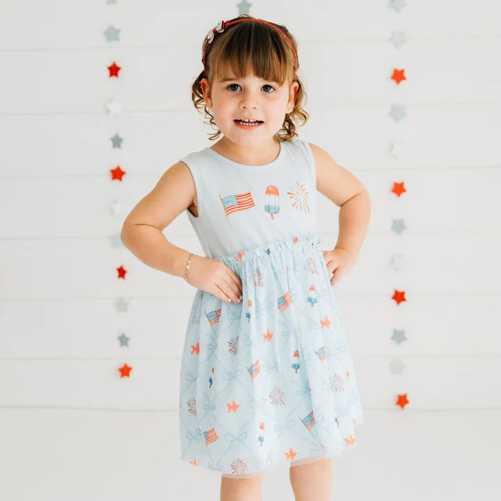 Model wearing a patriotic trellis tank tutu dress by Sweet Wink, featuring a glitter flag bow headband and vibrant red, white, and blue colors.