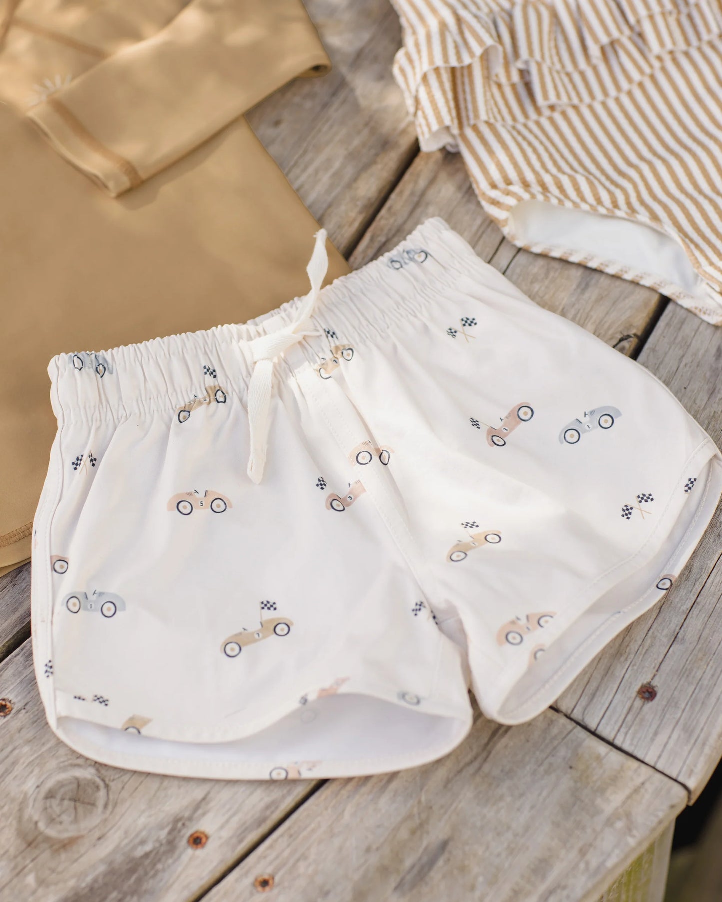 Boy wearing Quincy Mae race car boys swim shorts, featuring colorful race car print, casual summer swimwear for kids.