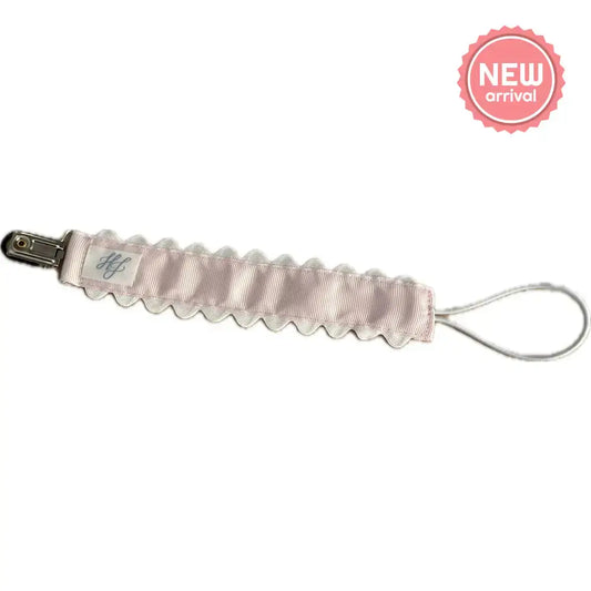 Hampton James Pink Paci Clip attached to a baby pacifier, featuring a soft pink fabric and a metal clip for easy attachment.