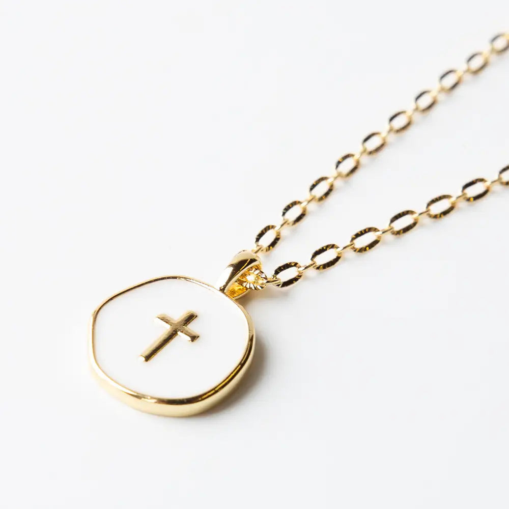 Lenny & Eva white enamel cross pendant on gold chain, faith over fear jewelry, close-up of religious necklace.