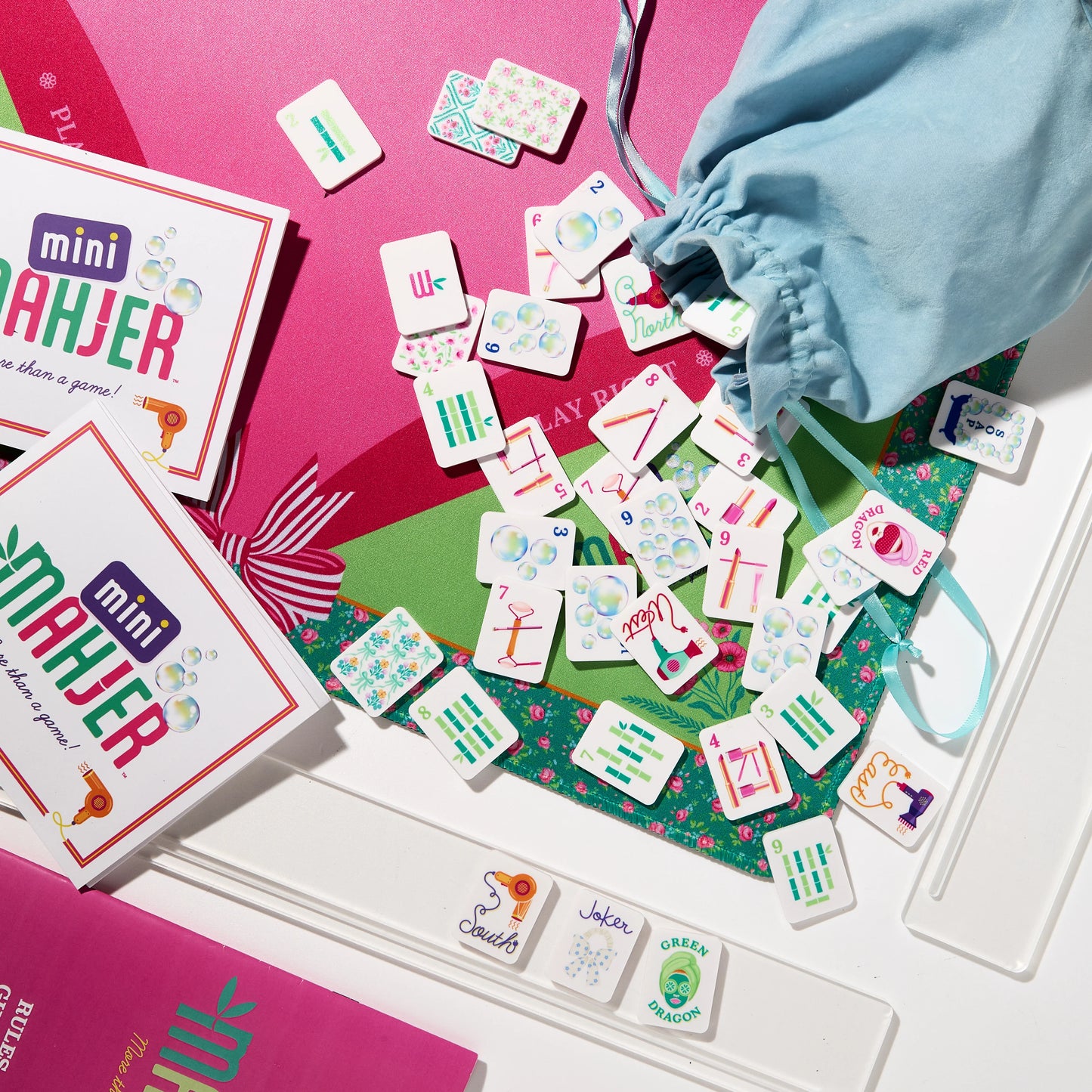 Mini Mahjer's Complete Game Bubbles & Bows Edition box with colorful game pieces and vibrant packaging on a gaming table.
