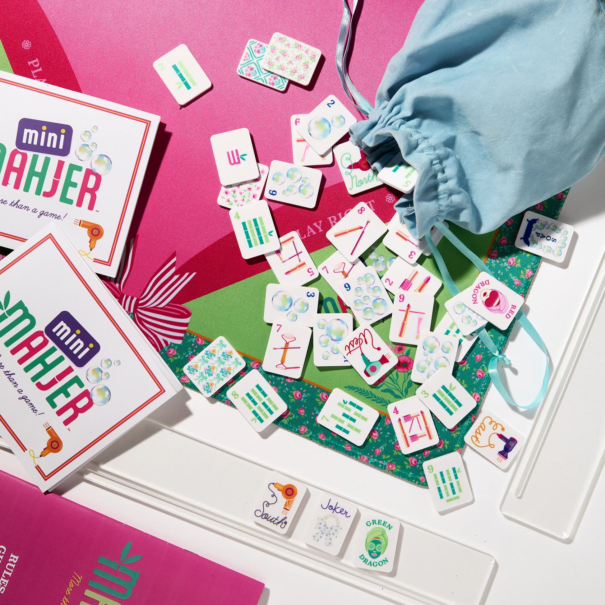 Mini Mahjer's Complete Game Bubbles & Bows Edition box with colorful game pieces and vibrant packaging on a gaming table.