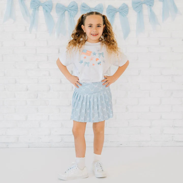Model wearing a white patriotic watercolor short sleeve T-shirt by Sweet Wink, featuring sky blue accents and flag-themed details.