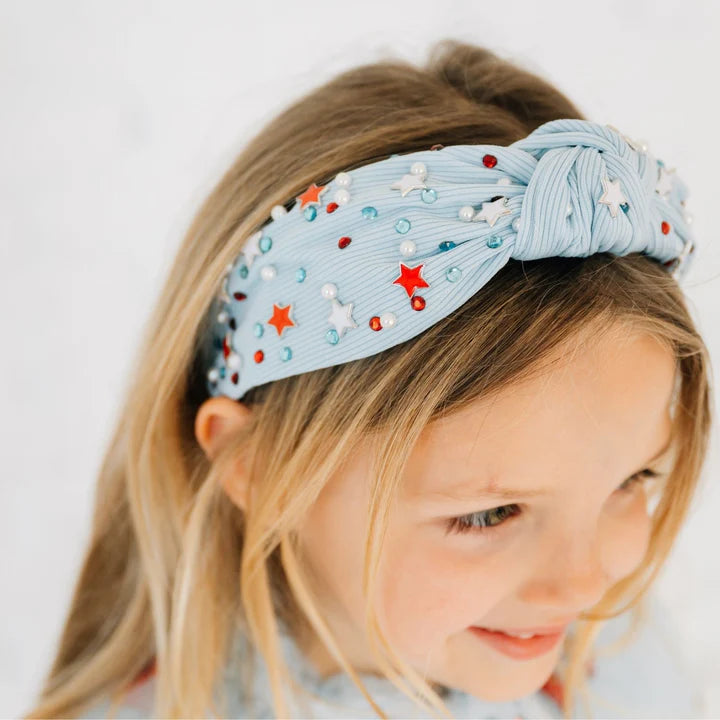 Model wearing a Sweet Wink USA Stars gemstone headband with blue and red star accents on a silver band.