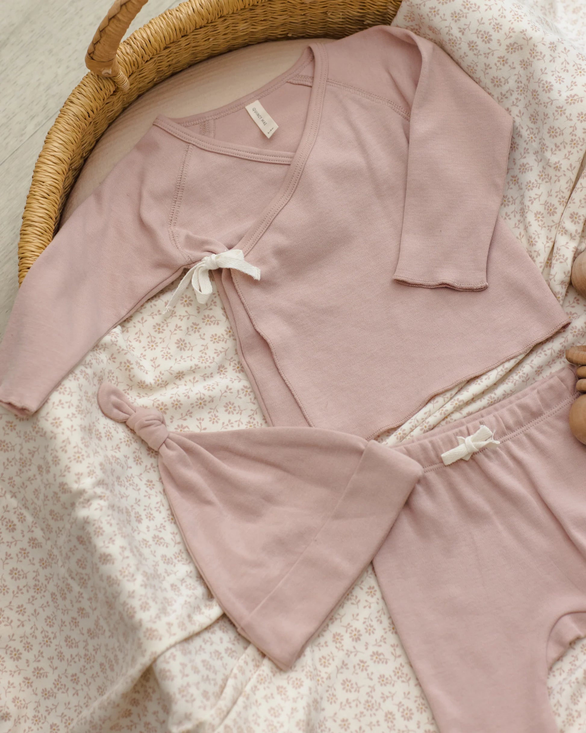 Baby girl wearing a blush pink knotted hat from Quincy Mae, styled in a cozy lifestyle setting.
