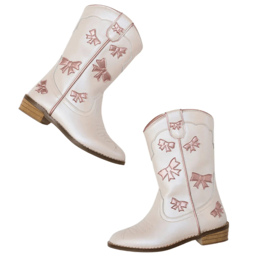 Wild + Rae cowgirl boots with white leather and pink bow accents, featuring a pointed toe and Western-style heel.