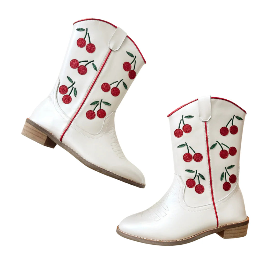 Wild + Rae Cowgirl Wild Cherry Boots featuring red leather, pointed toes, and Western stitching on a wooden floor background.