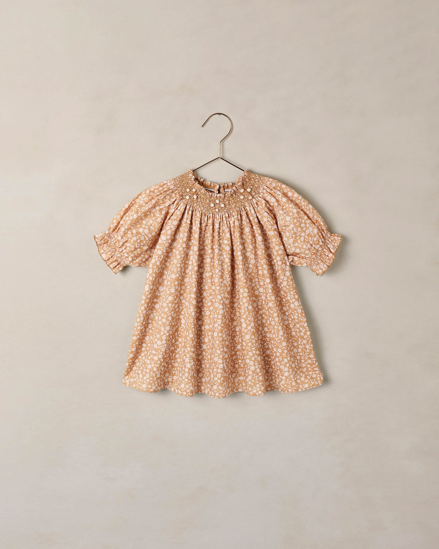 Noralee Golden Meadow Maddie Dress hanging on a hanger with floral pattern and flowing fabric, perfect for warm weather.