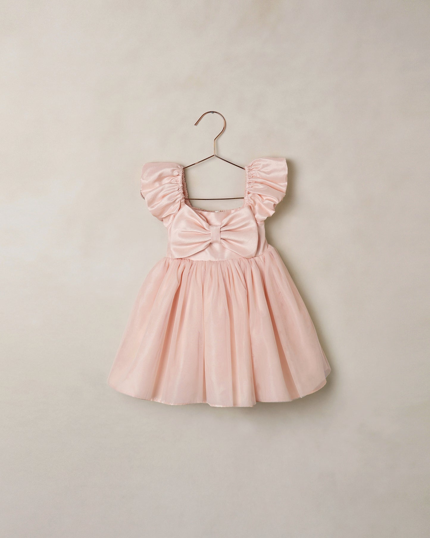 Noralee Blush Madeline Dress displayed hanging on a wooden hanger with a soft fabric texture and elegant design.
